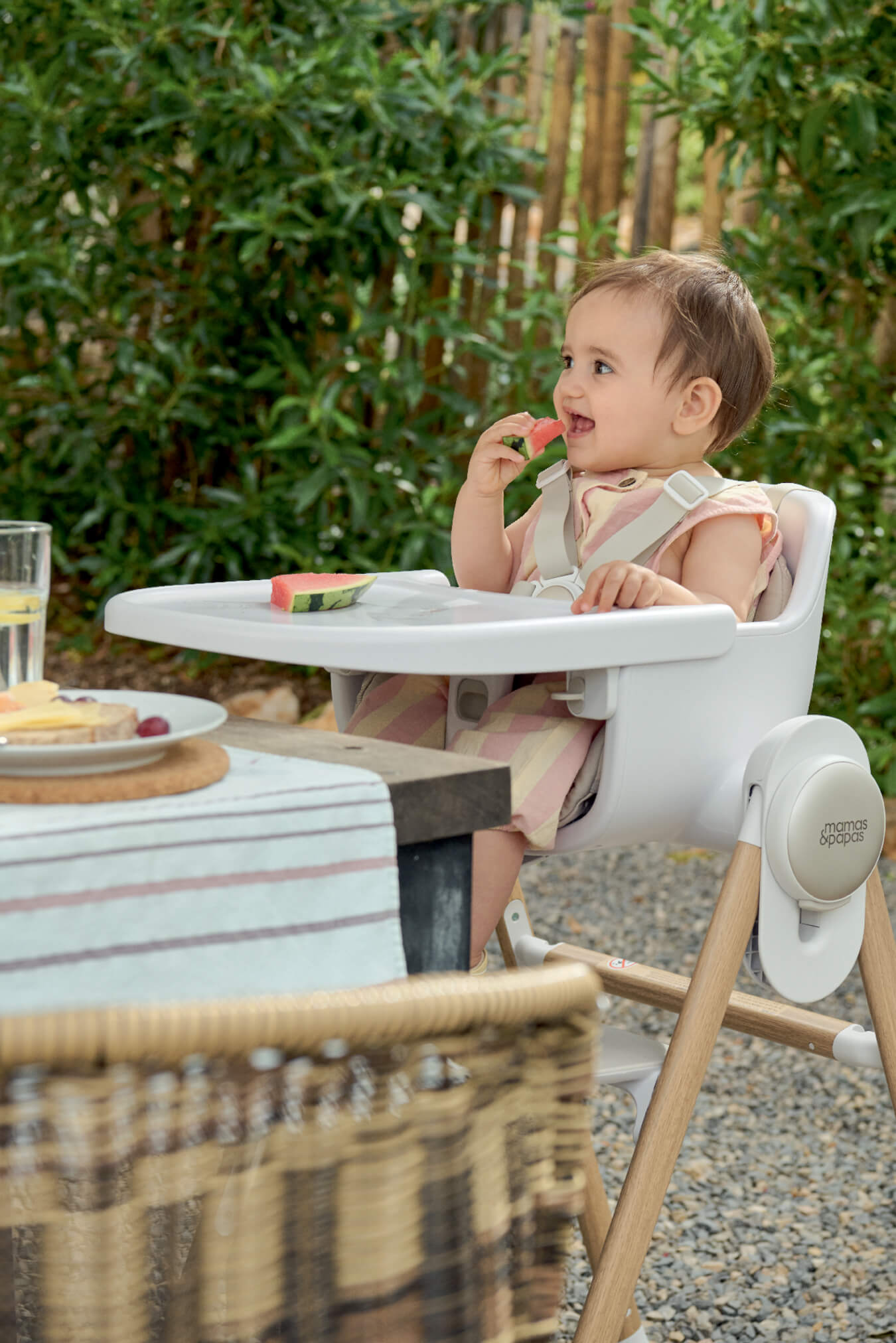 A child sitting in a high chair, eating fruit outdoors.