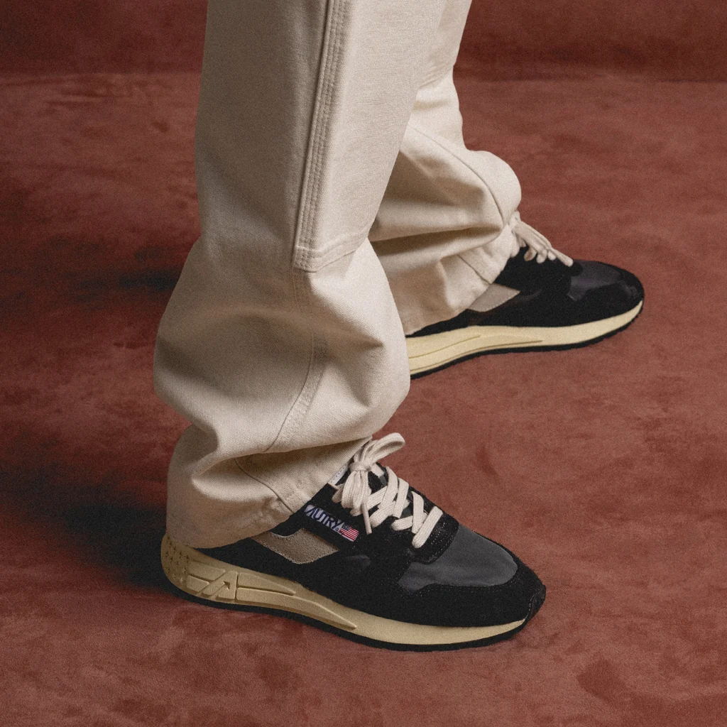 Person wearing black and beige sneakers with cream-colored pants on a brown background.