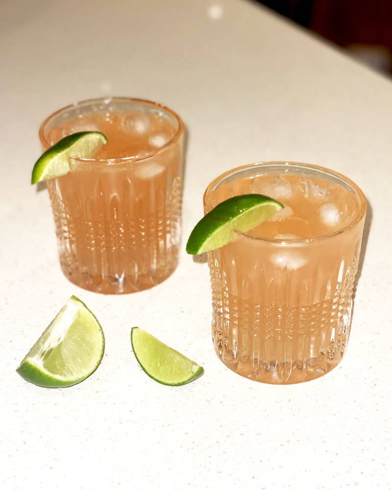 Two Paloma cocktails on kitchen bench with lime wedges