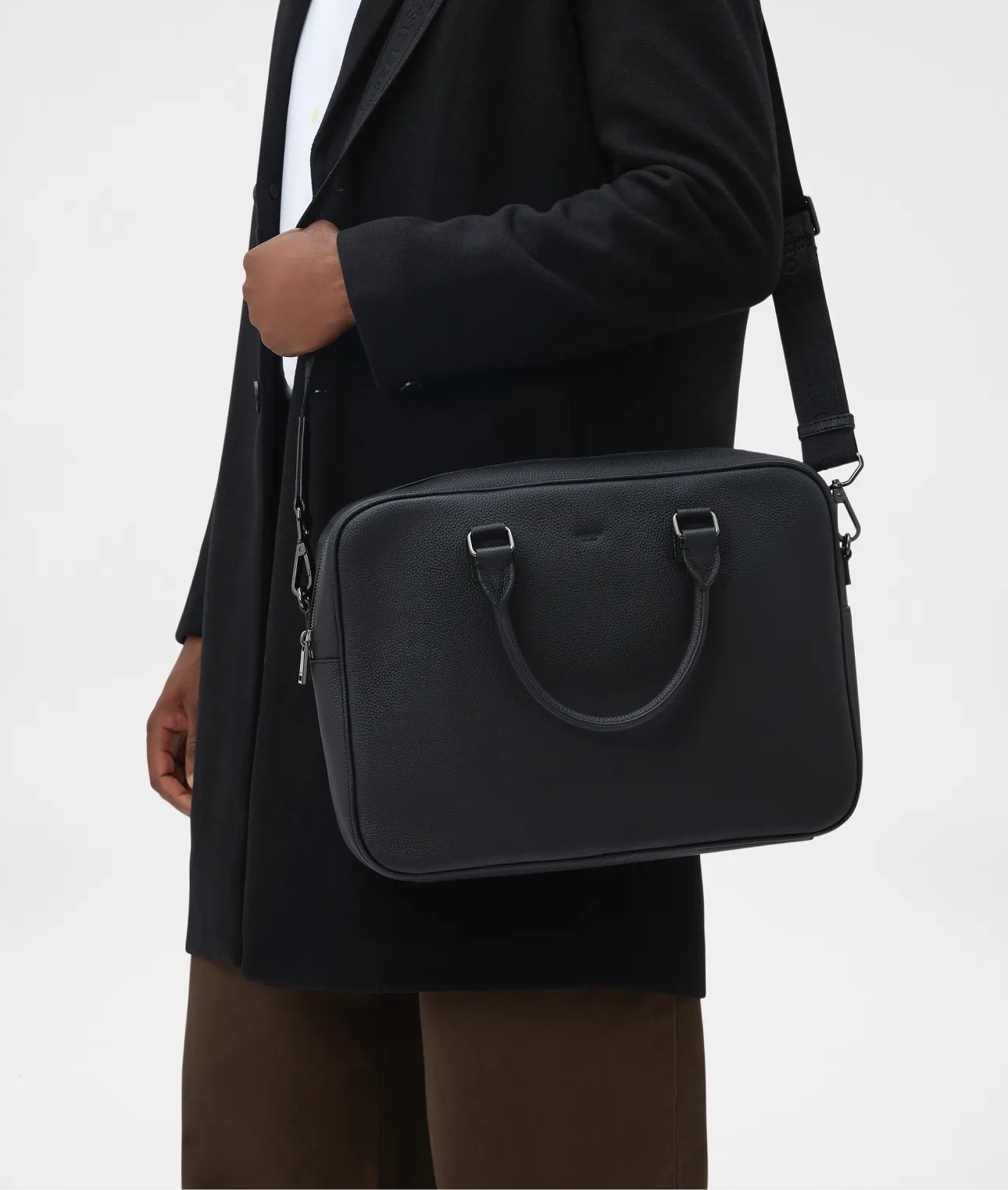 A person holding a black leather bag while wearing a coat.