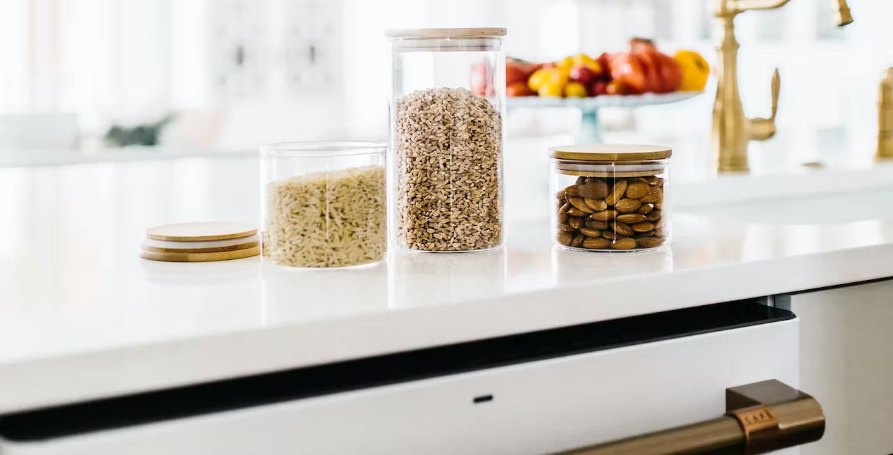 Grains and nuts in glass storage containers on counter above dishwasher