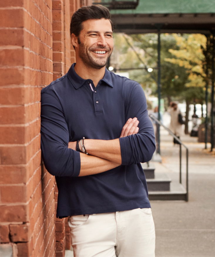 Smiling man in a navy polo shirt leaning against a brick wall.
