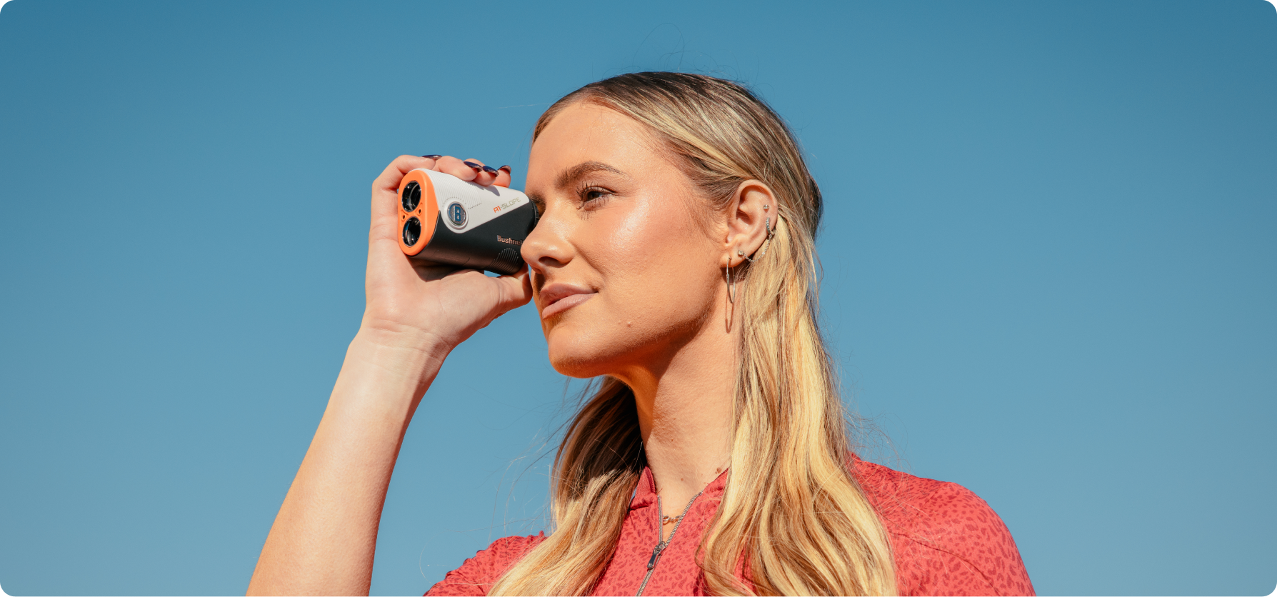 A woman holding a camera against a clear blue sky.