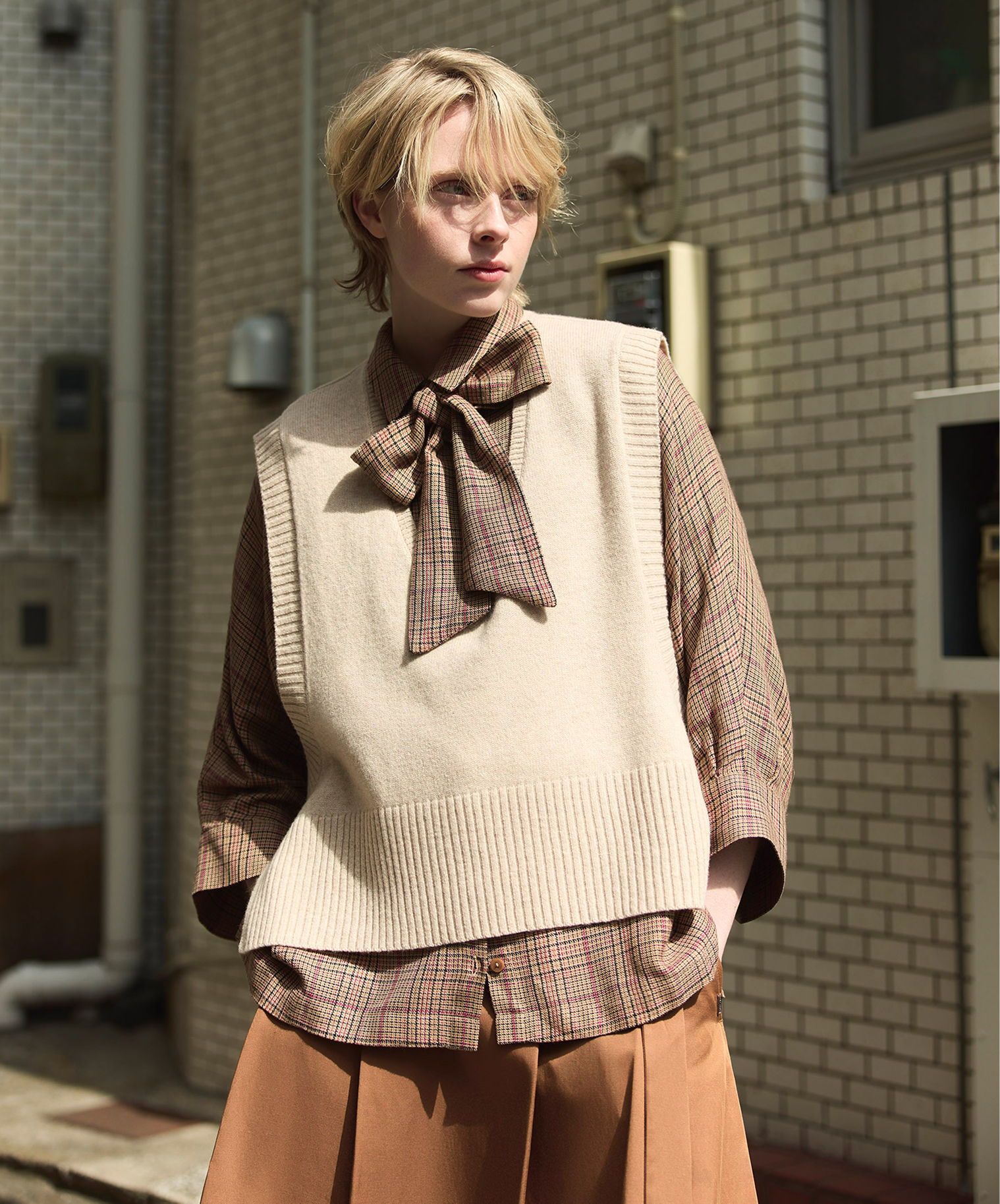 Model wearing a vest over a shirt, posed in an urban setting.