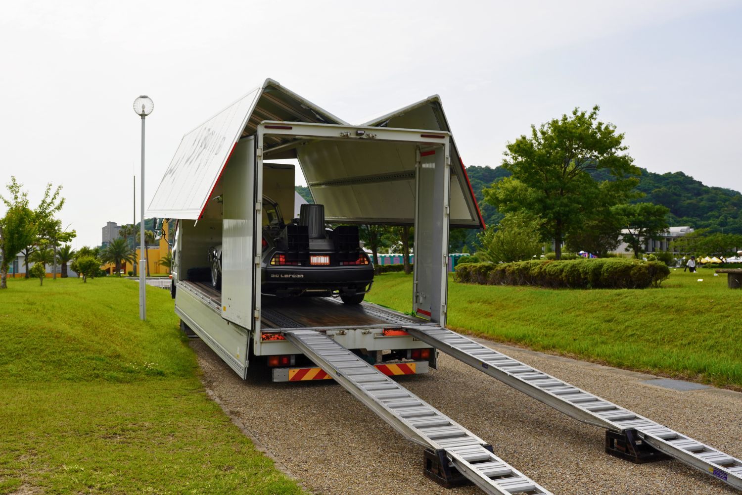 Truck with ramps parked on grass, partially open at the back.