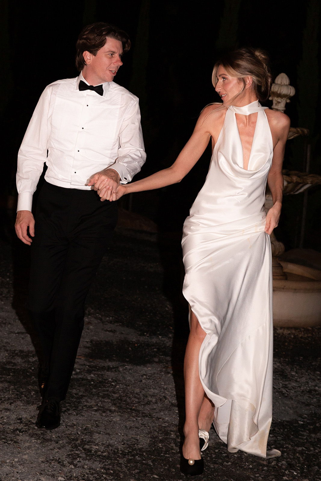 A couple dressed elegantly walking hand in hand at night.