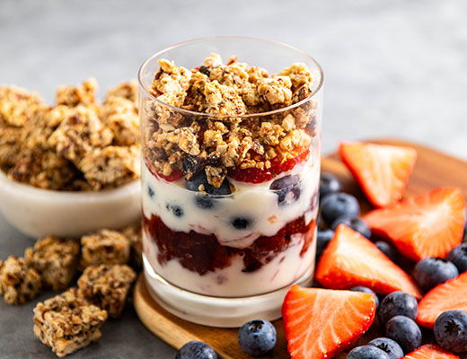 Layered yogurt parfait with berries and granola on a wooden plate.