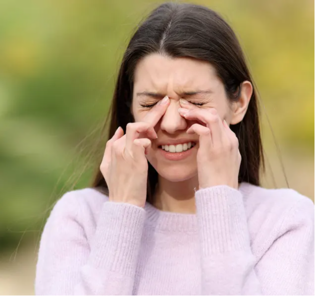 Žena v bolesti si tlačí na koreň nosa. Injekcie na alergie môžu pomôcť zmierniť príznaky alergickej nádchy, ako je upchatý nos.