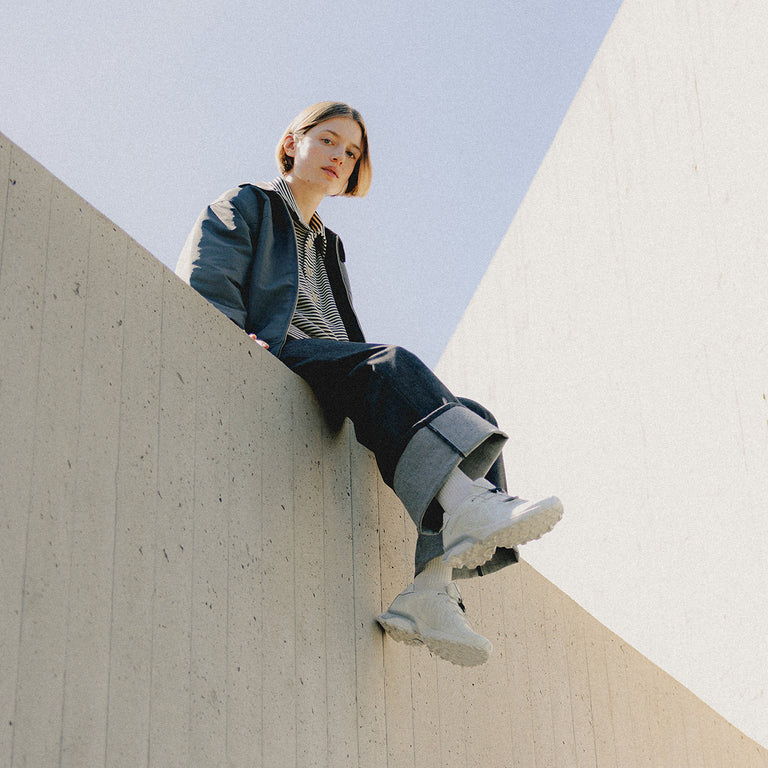 Person sitting on a concrete ledge, wearing a jacket and boots.