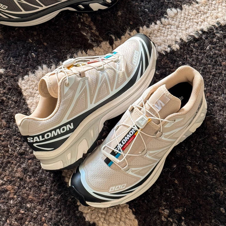 A pair of beige Salomon sneakers on a patterned rug.