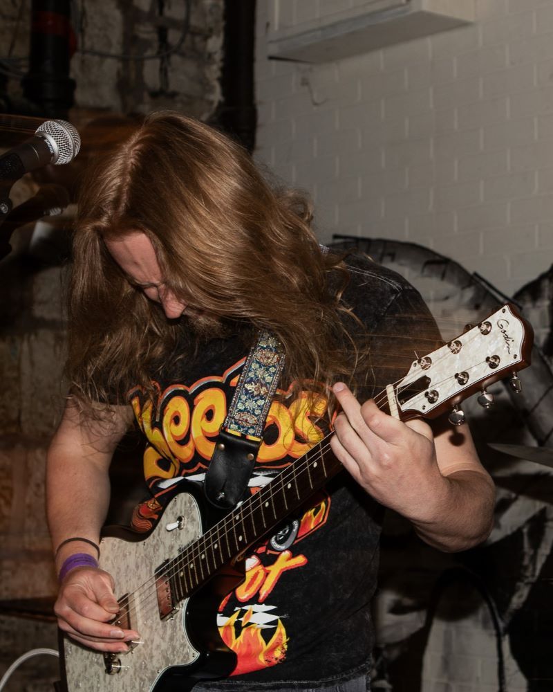 Person with long hair playing electric guitar on stage.