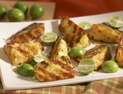 Grilled pineapple slices with lime wedges on a white plate.