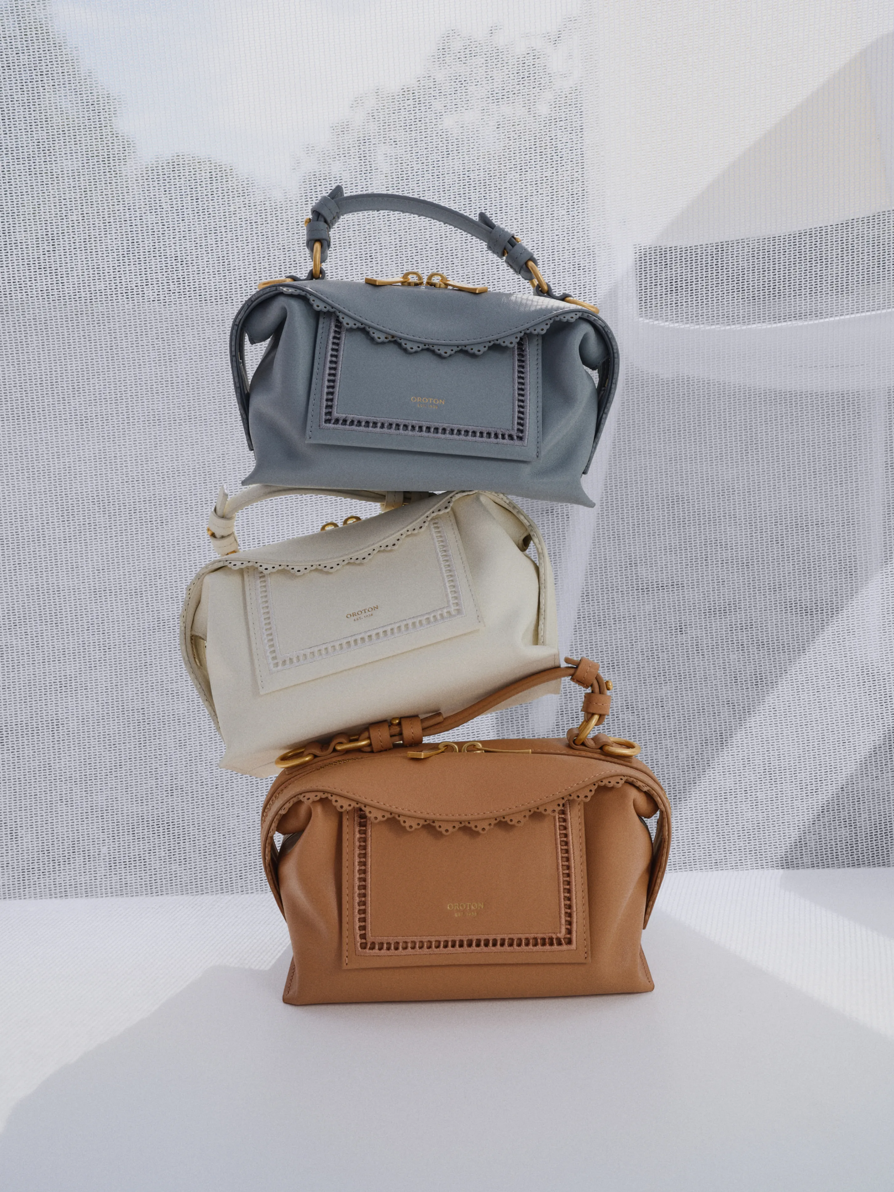 Three stylish handbags in gray, white, and brown stacked together.