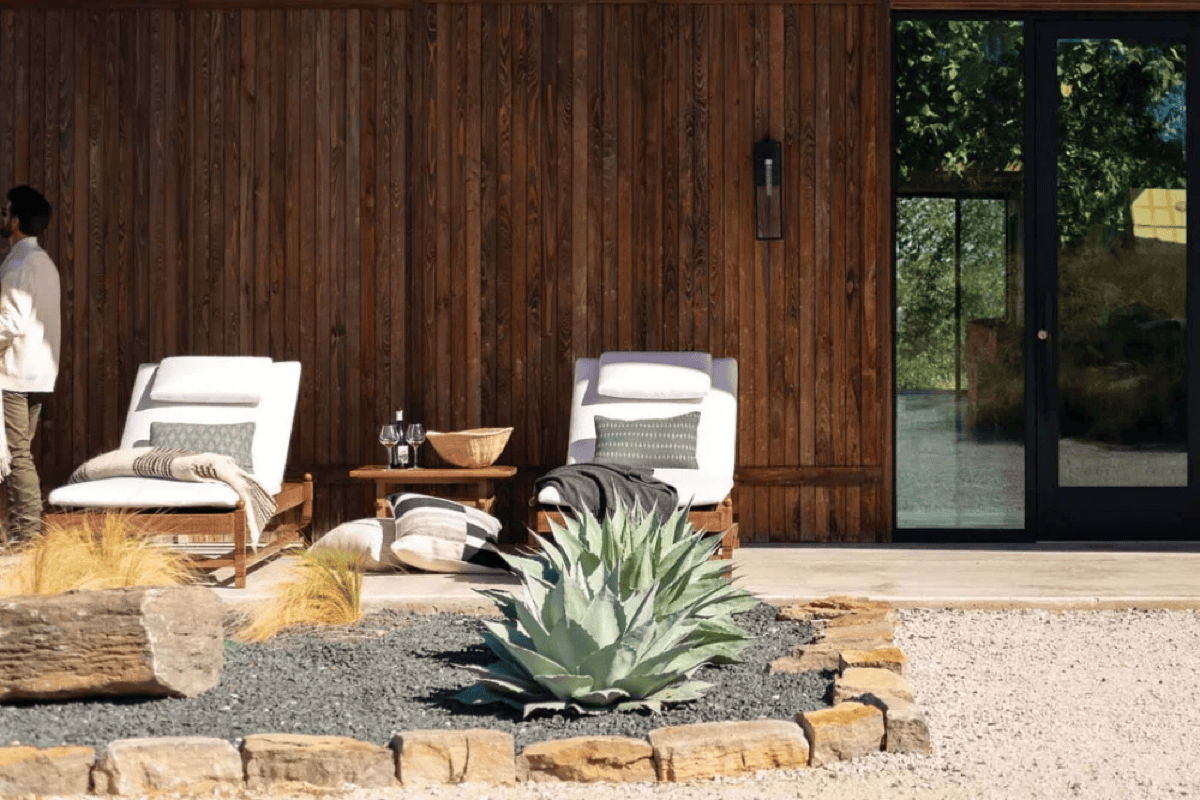 Modern patio with outdoor chaise lounges, wood siding, desert plants, and gravel landscaping, showing durable outdoor furniture in a natural desert setting.