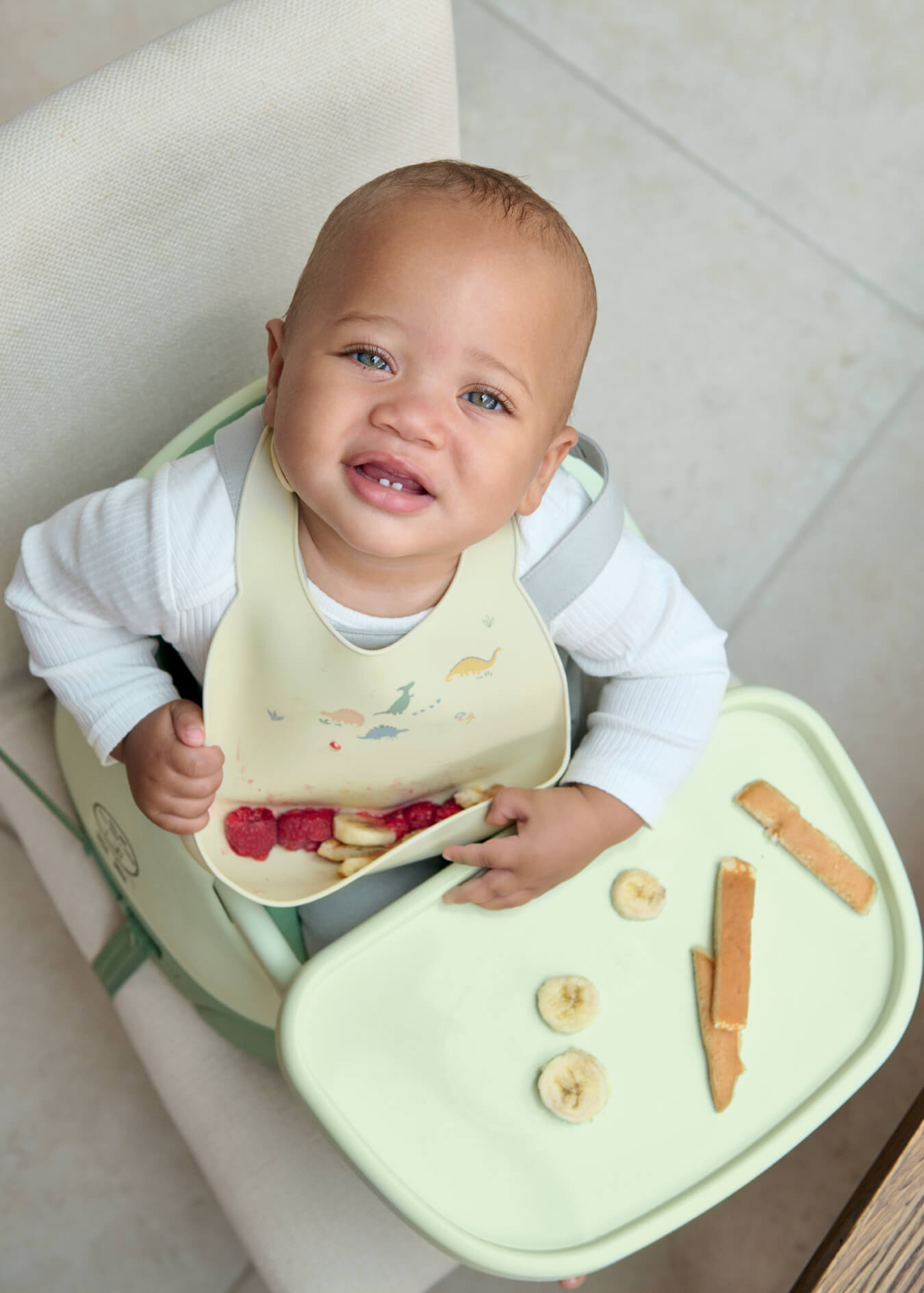 Smiling baby in a high chair with food on the tray.