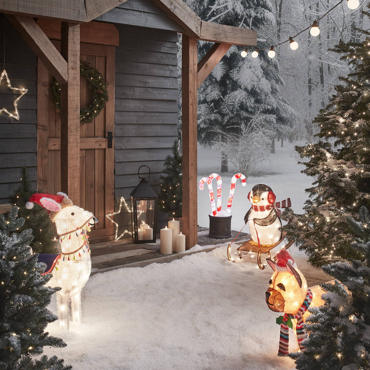 Alpaca, bulldog and penguin trio standing in a wintery garden in front of a cosy cabin