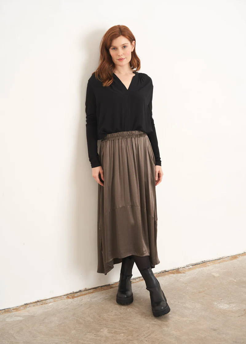 A model weaing a black long sleeved top with a khaki brown midi satin skirt with black chunky boots