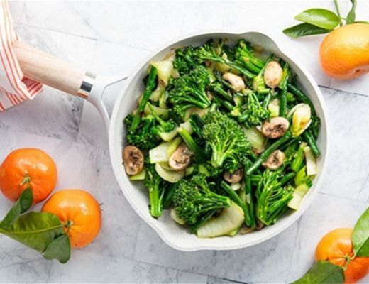 Bowl of sautéed greens and mushrooms with tangerines on a marble surface.