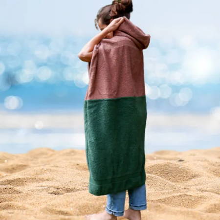 woman walking on the beach putting on the hood of a beach poncho made out of towels