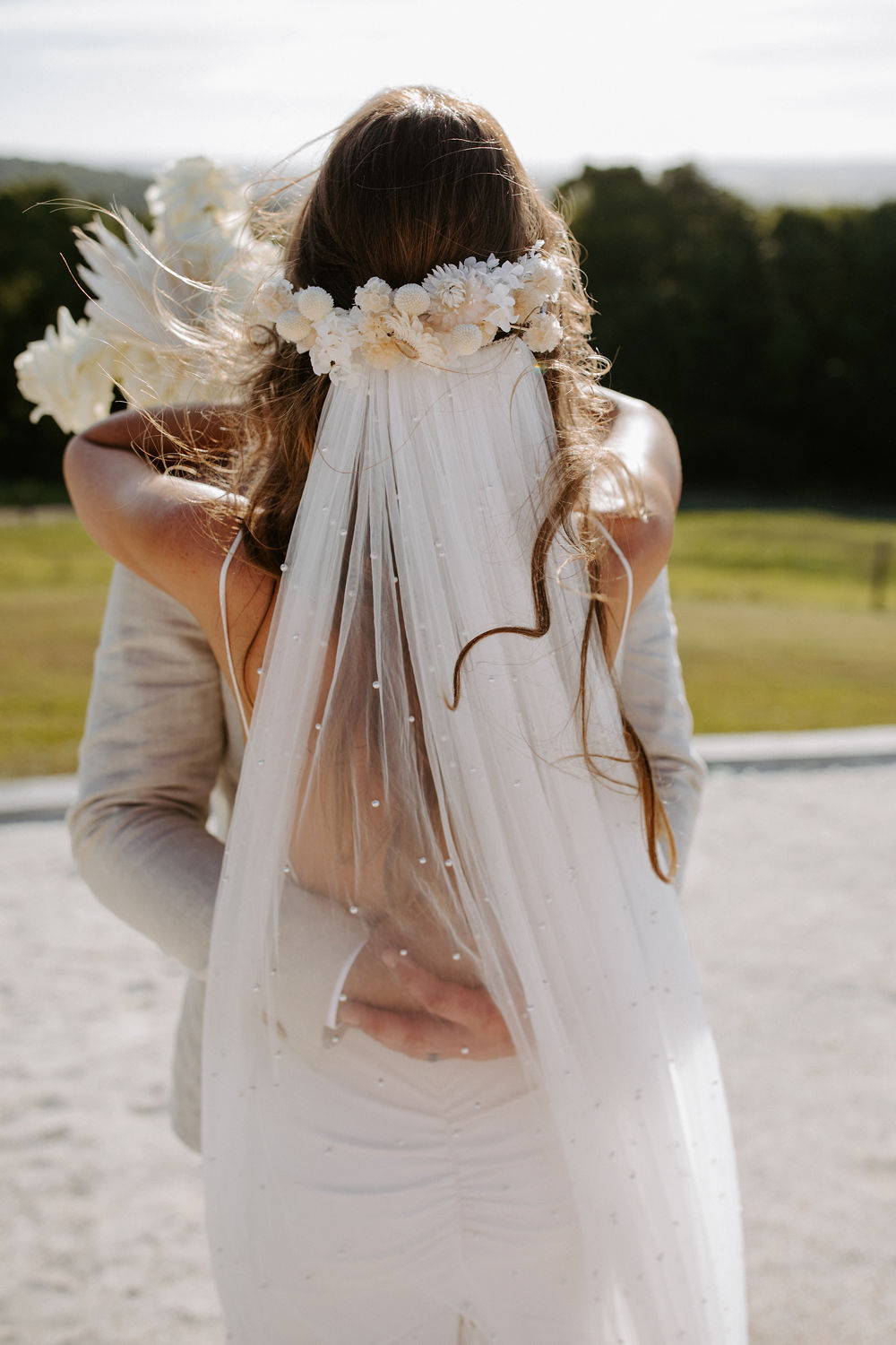 Die Braut trägt den langen, perlmuttfarbenen Schleier von Grace Loves Lace und umarmt ihren neuen Mann