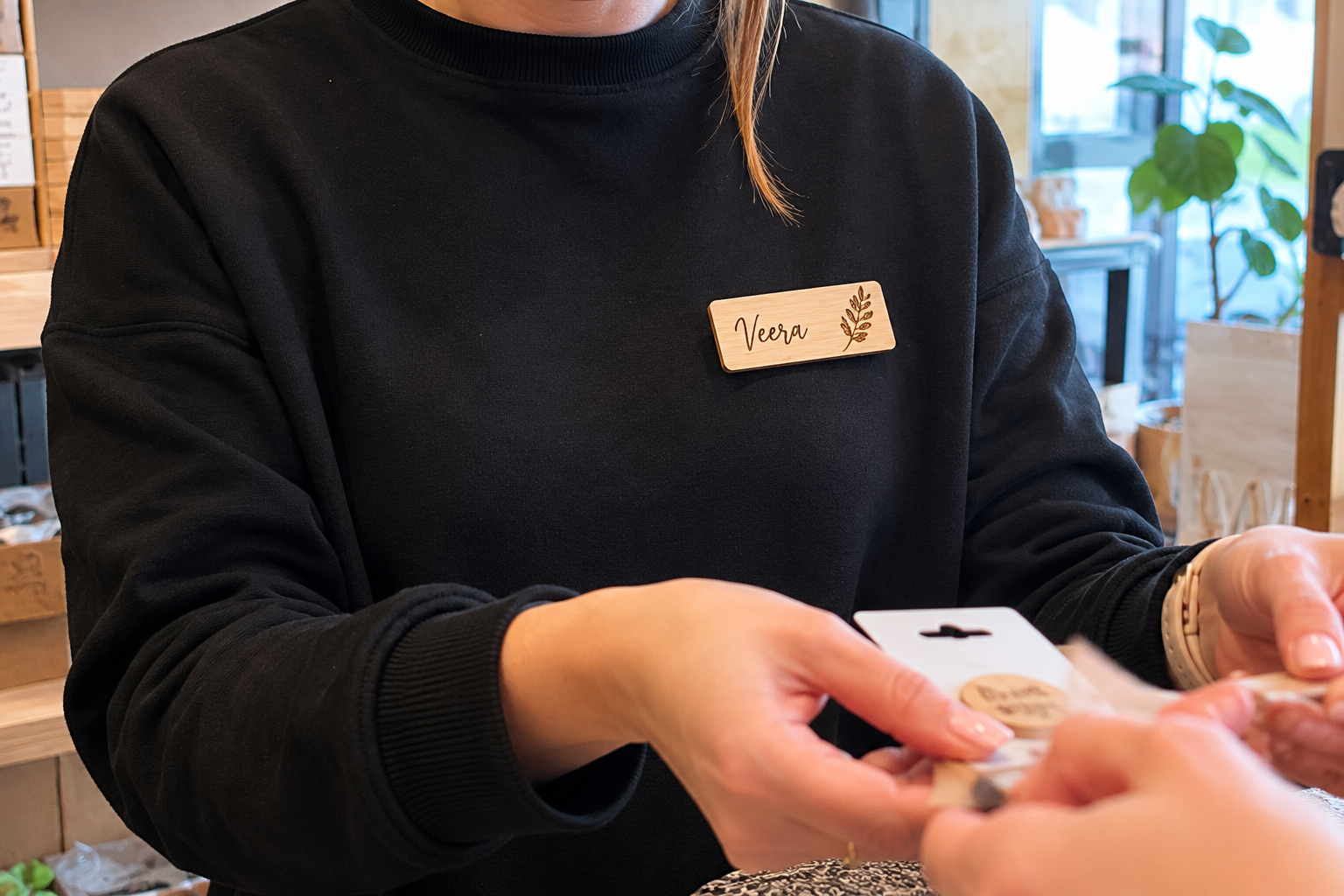 Henkilökunnan puinen nimikyltti asiakaspalvelutilanteessa