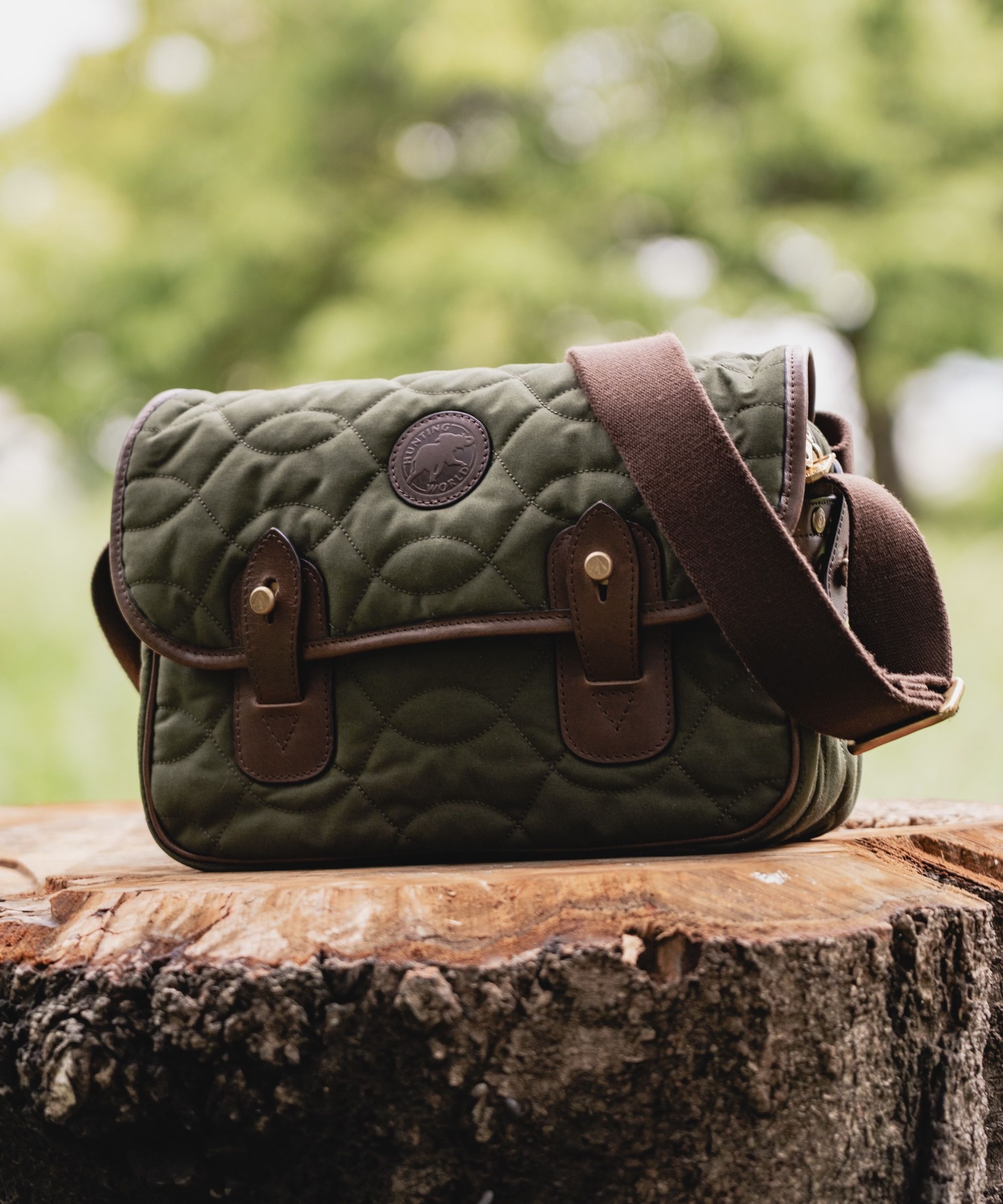 Quilted green messenger bag resting on a wooden stump outdoors.