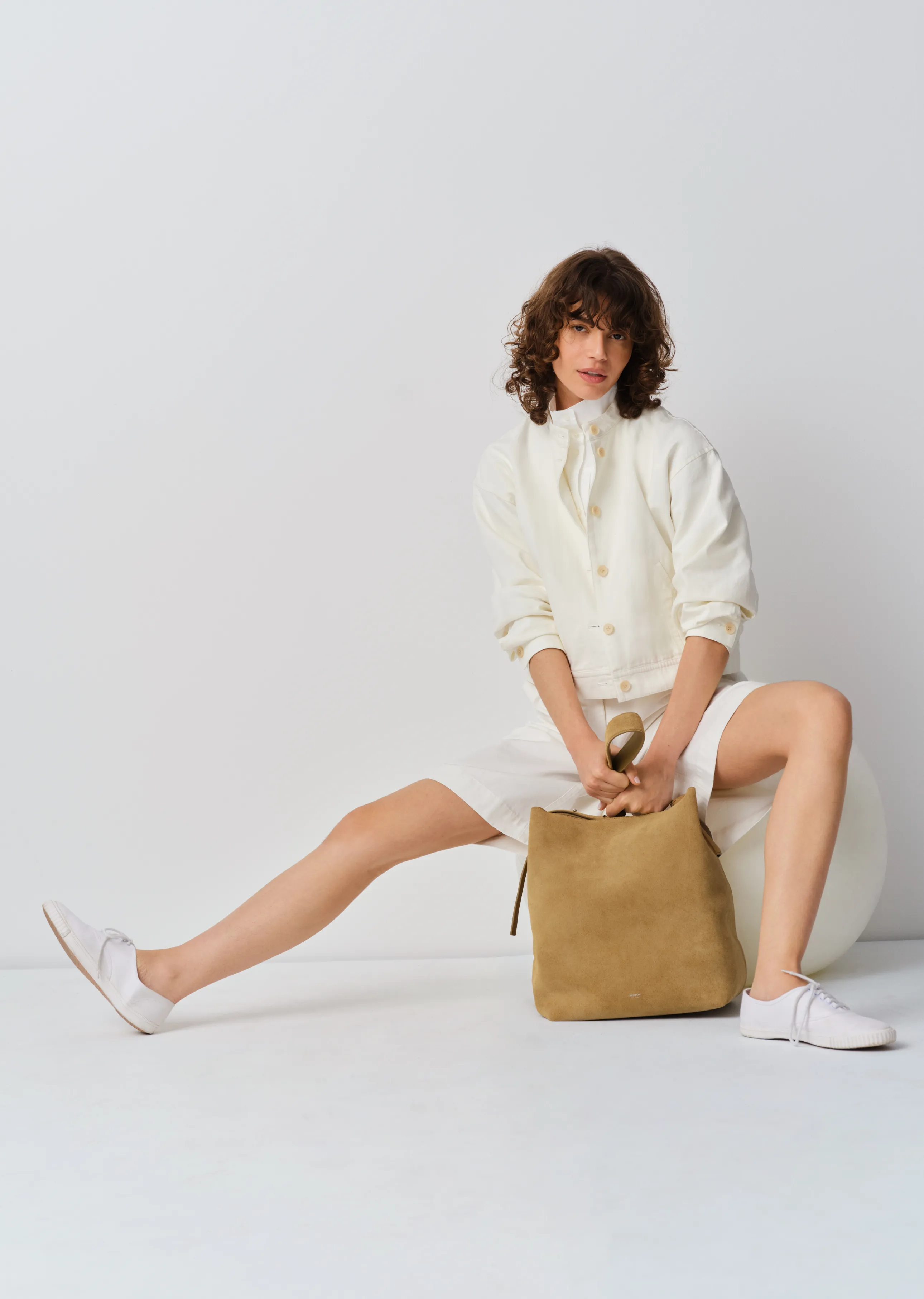 A woman in a white outfit sitting with a brown backpack.