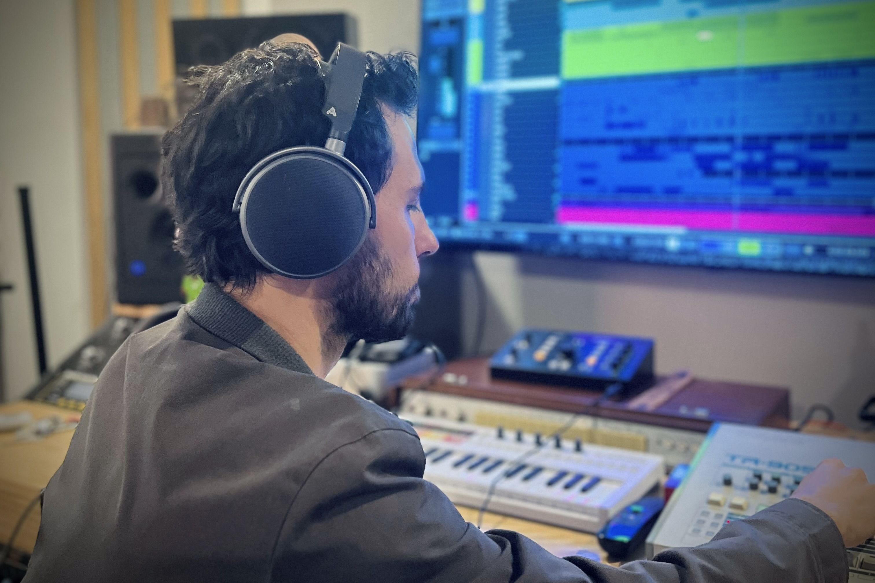 Andrew Guerrero wearing Audeze LCD-S20 headphones working on music production with a computer and synthesizer.