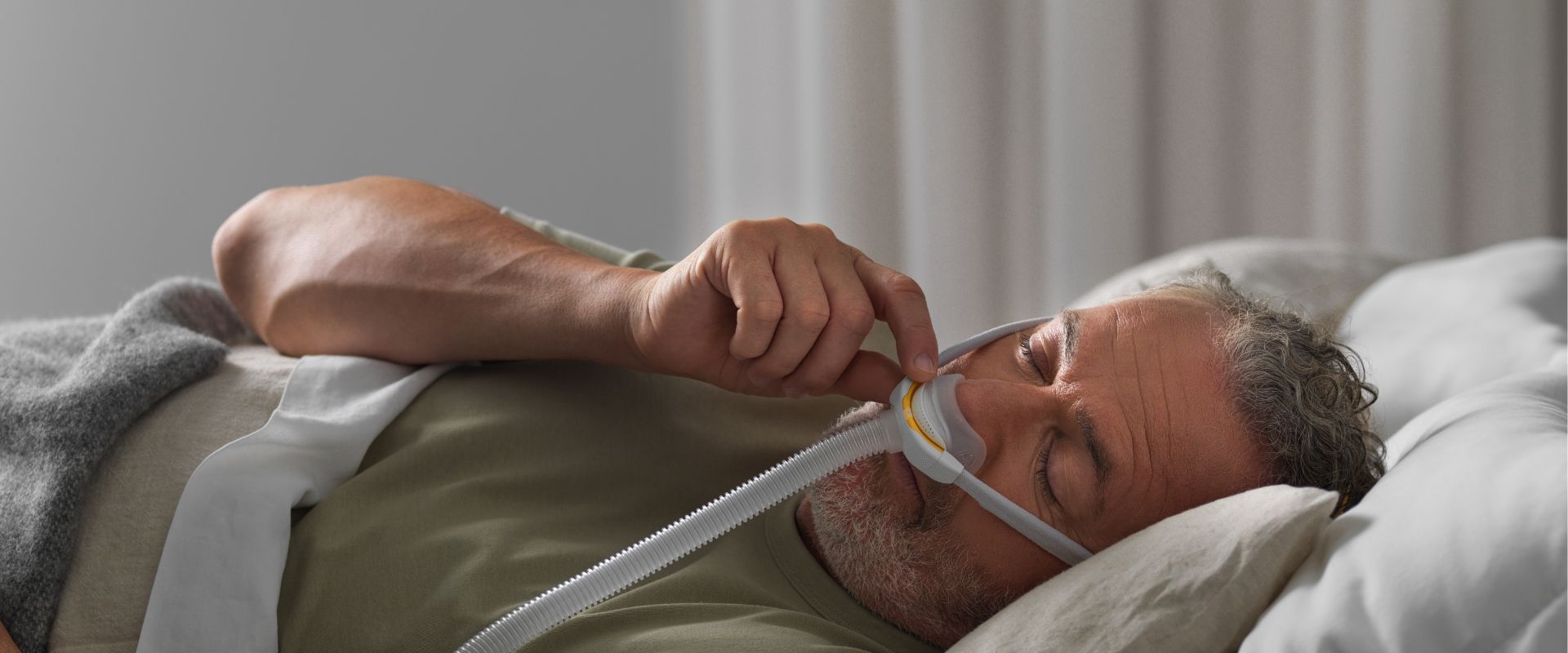 Elderly man sleeping with a CPAP machine in a bedroom setting.