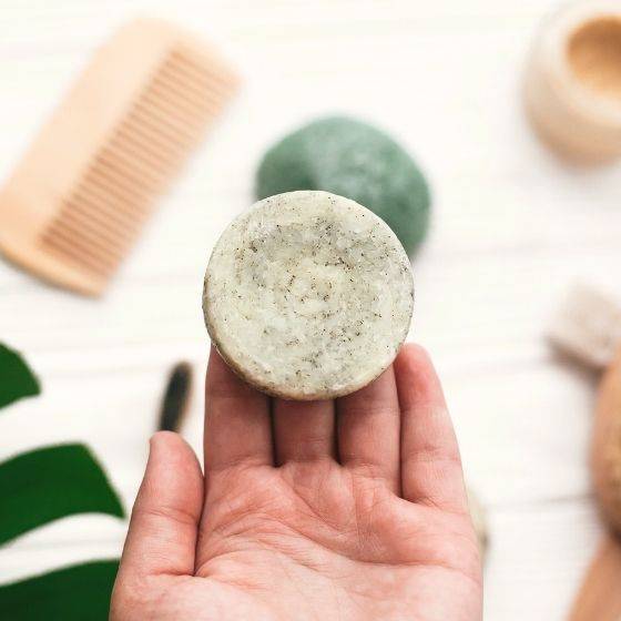 Hand holding green shampoo bar with hair brush and sponge visible in background