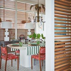 Wooden slat dividers in a dining room with a  white table and red upholstered chairs.