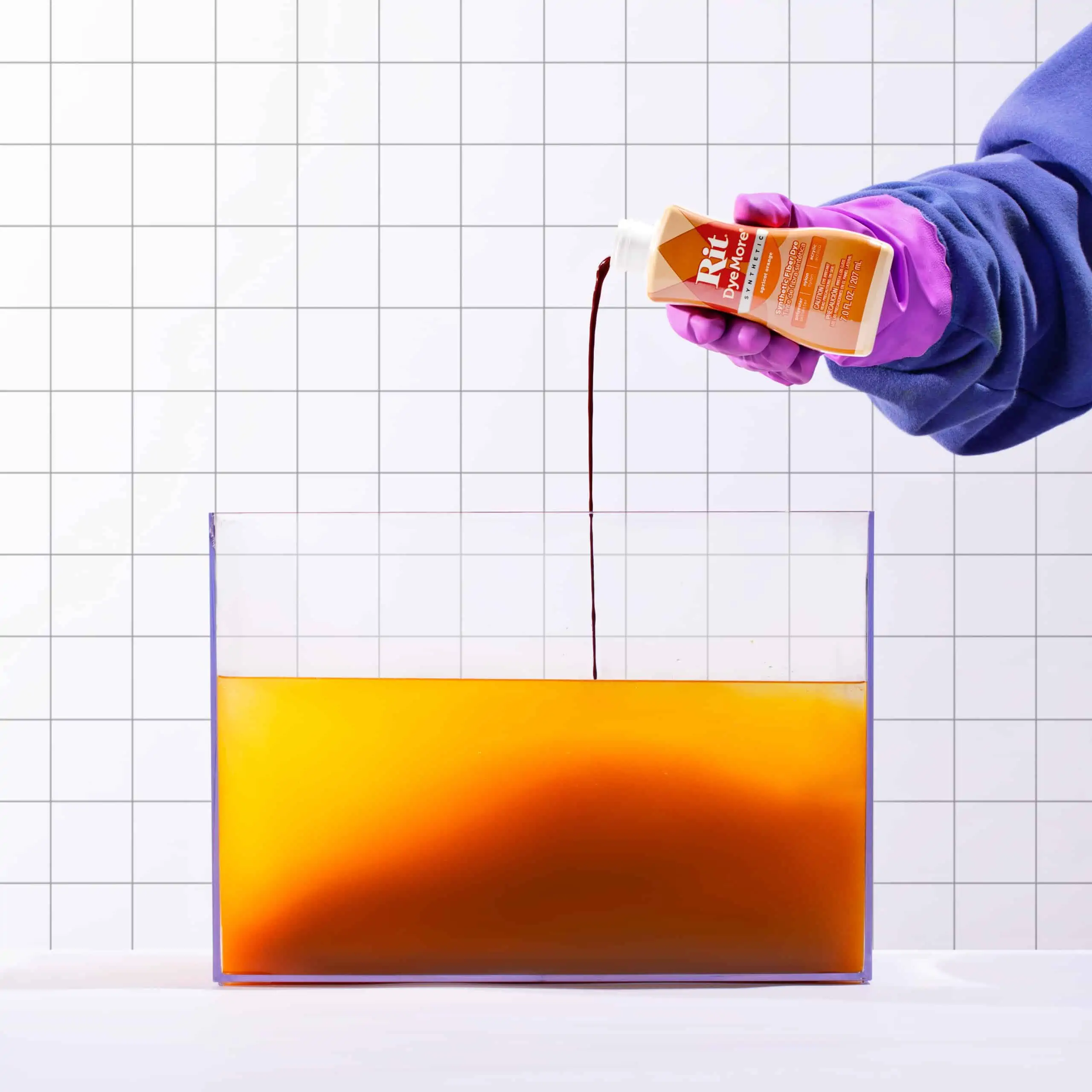 A hand pouring liquid into a transparent container filled with orange liquid.
