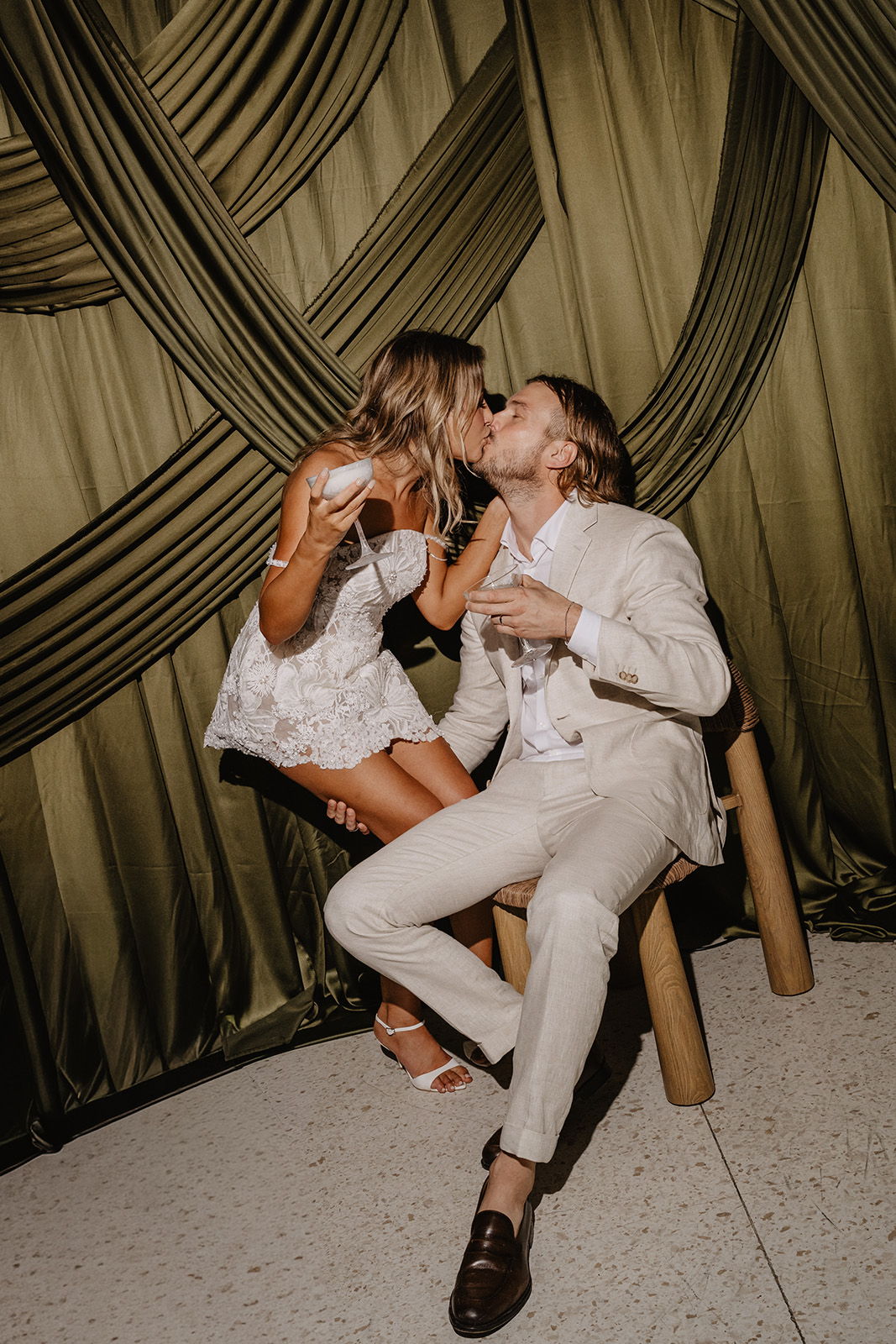 Couple kissing while seated, surrounded by draped fabric backdrop.