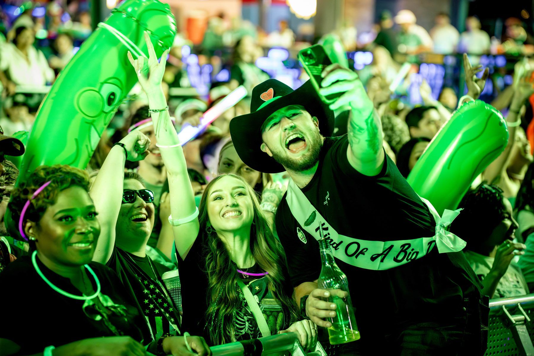 Crowd at the Pickle RAVE with inflatable pickle and a guest in a cowboy hat with a Kind Of A Big Dill sash at The Big Dill Arlington Texas 2025.