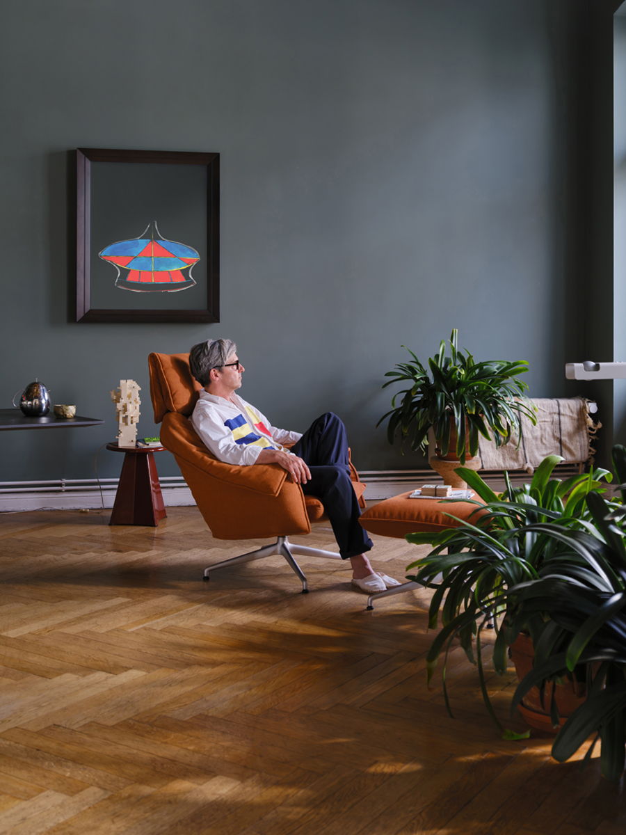 Person relaxing in a modern Bascule chair surrounded by plants and artwork.