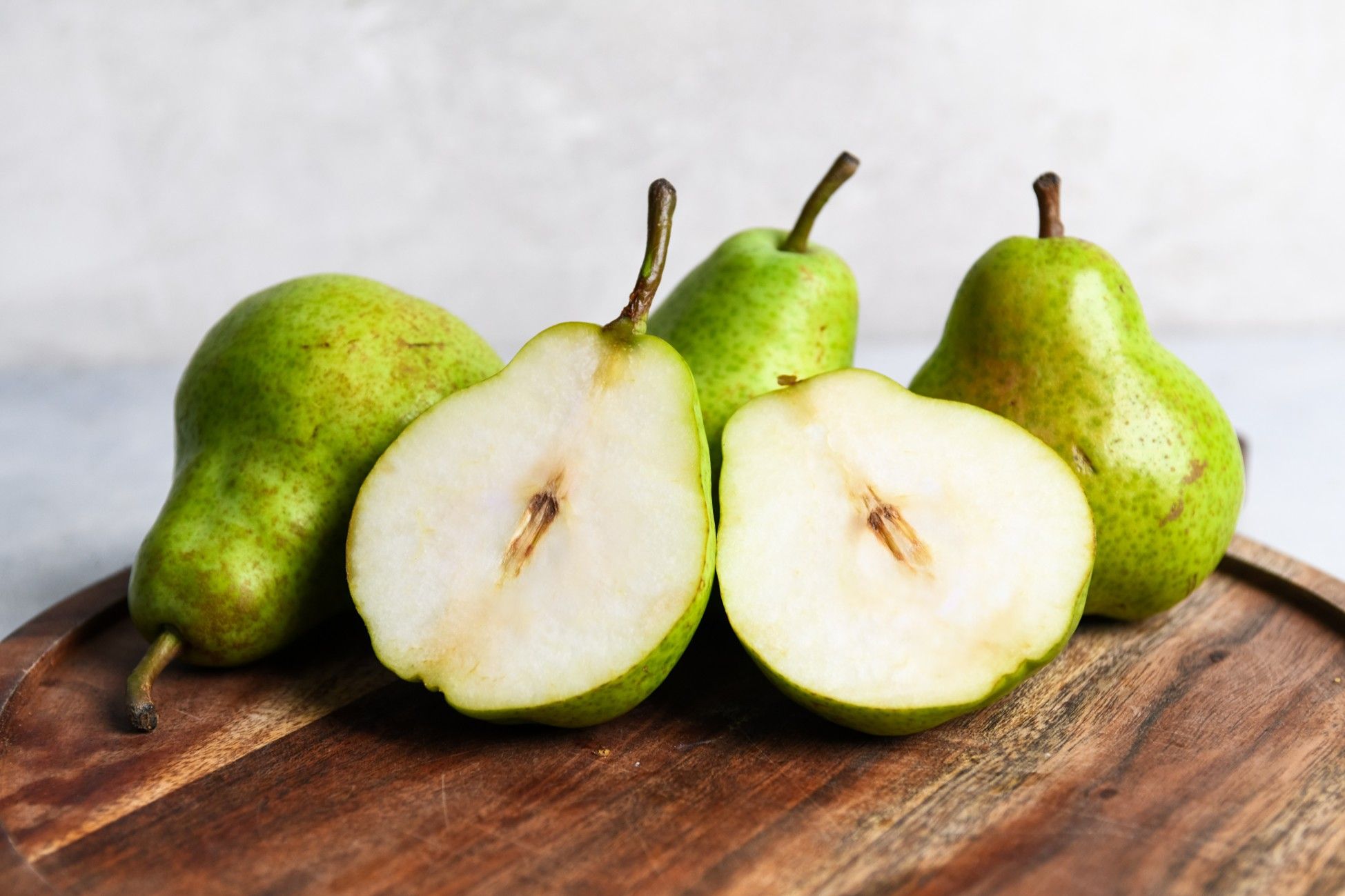 Fresh green pears, some whole and one cut in half, on a wooden board.