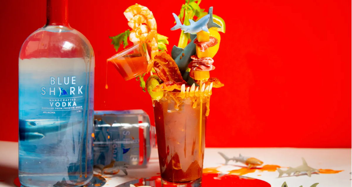 A colorful cocktail with garnishes, next to a bottle on a red background.