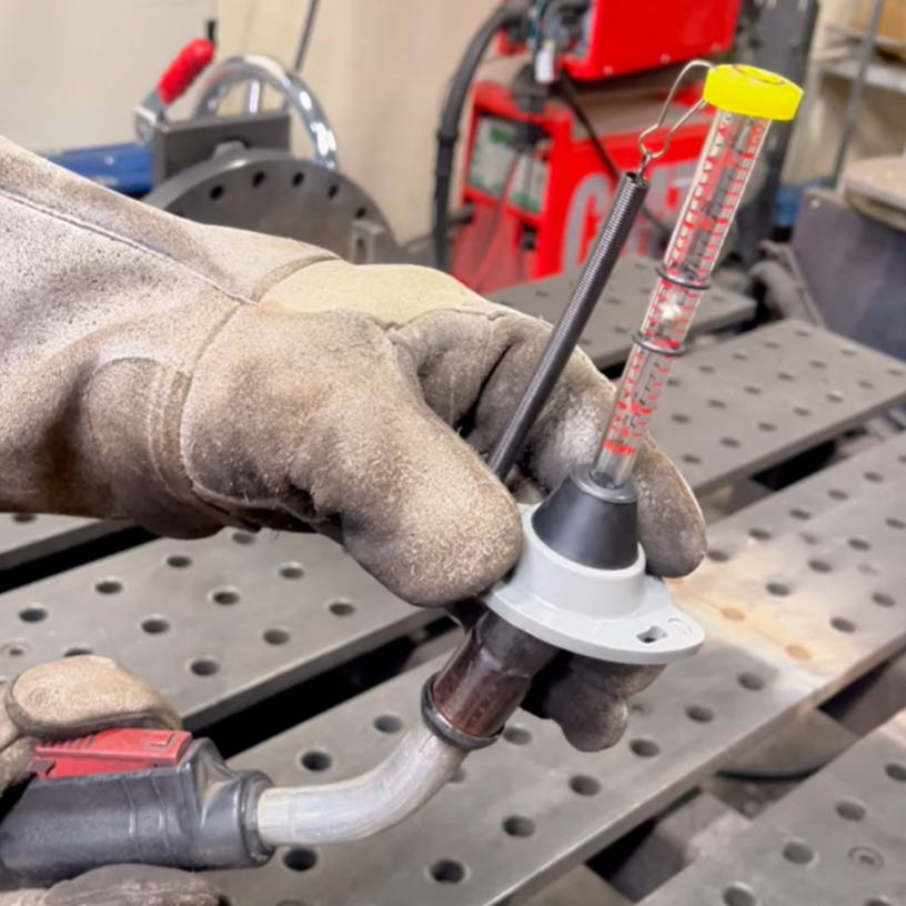 Person wearing gloves holding a tool with a measuring device in a workshop.