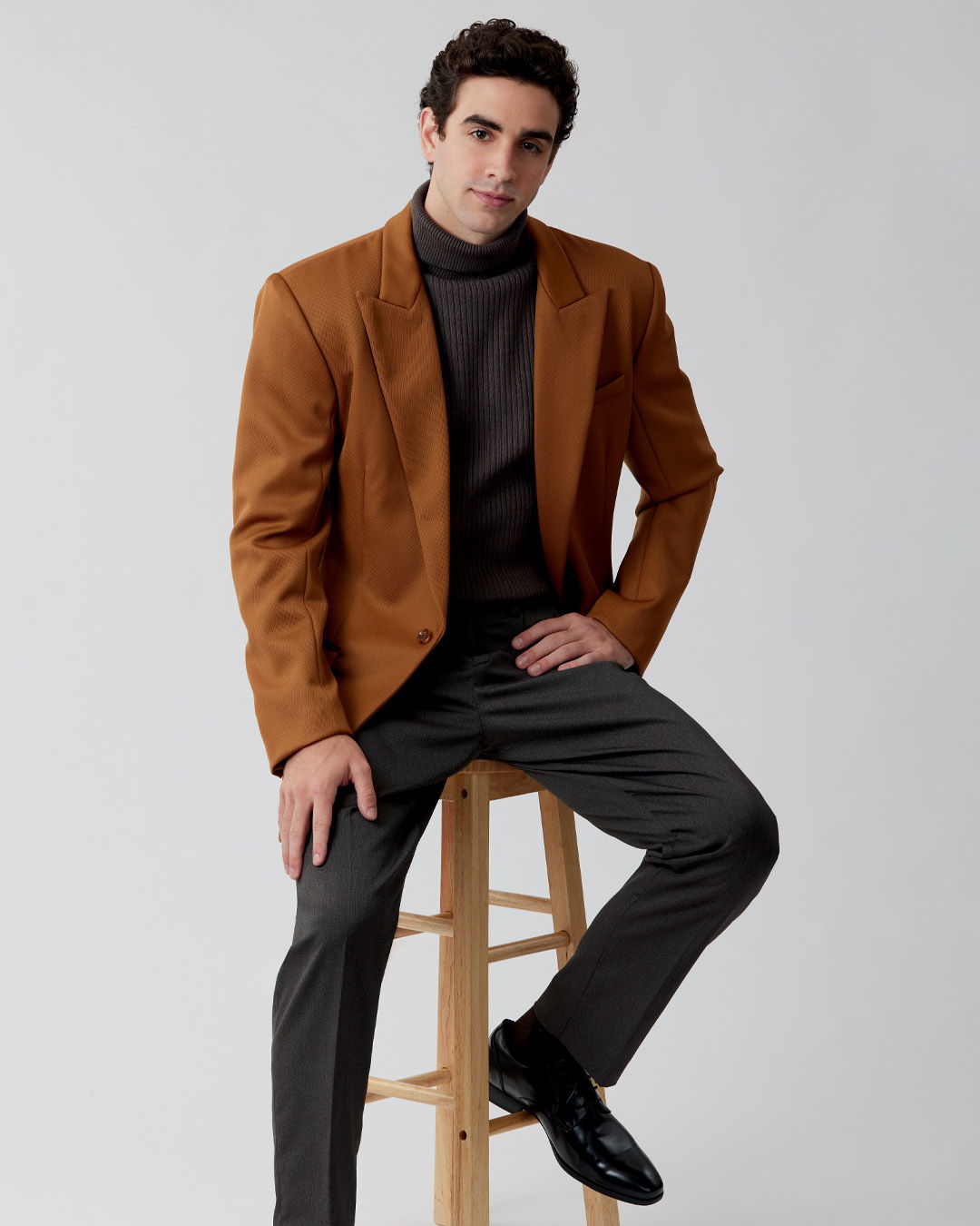 Man in a brown blazer sitting on a stool.