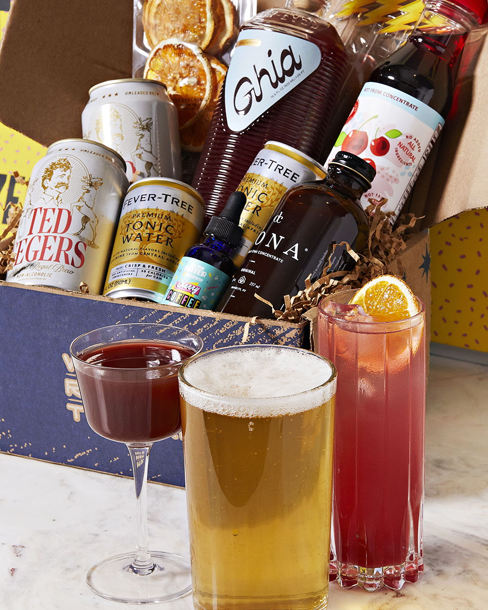 Three drinks in front of a box full of cocktail ingredients