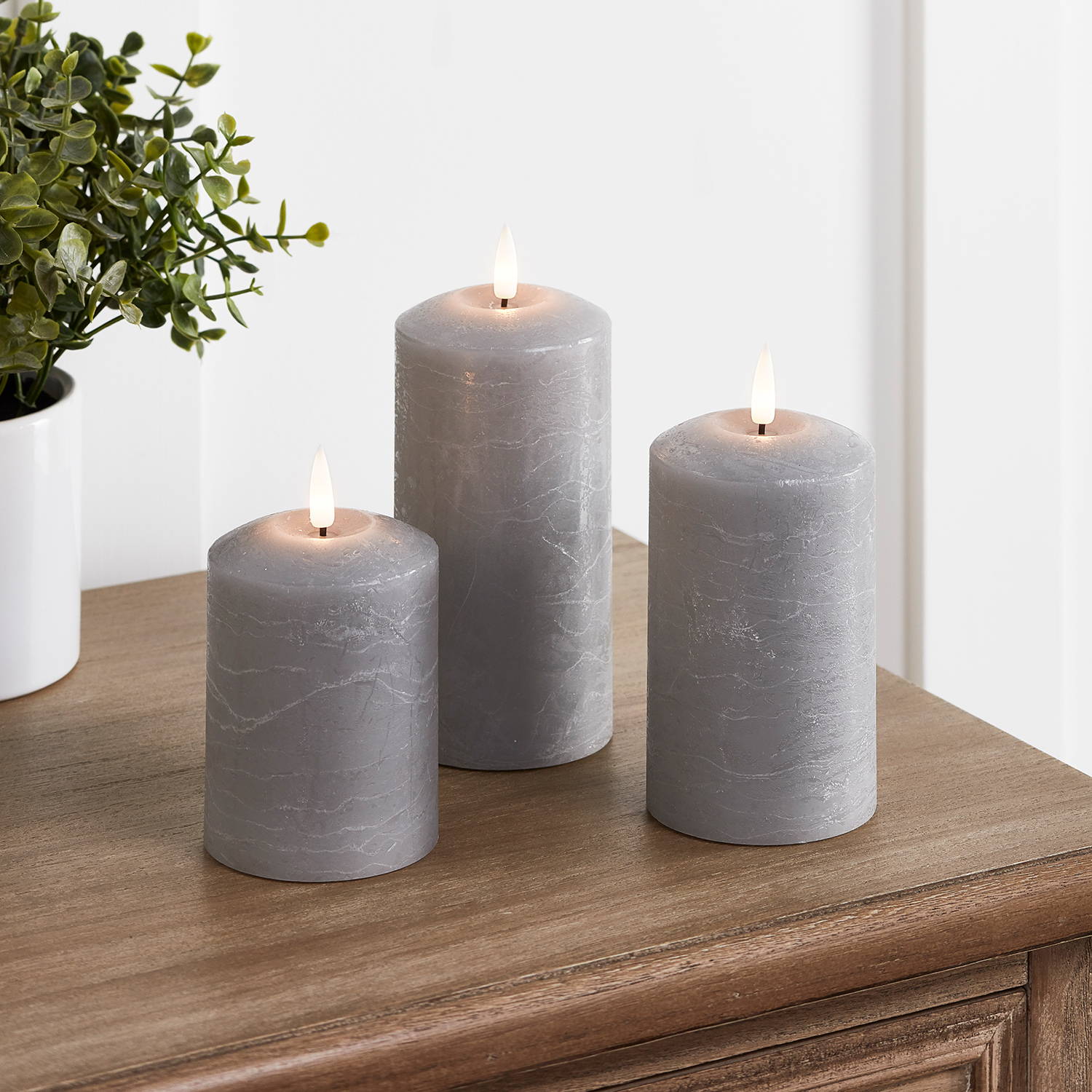 3 Grey candles on a side table with a plant.