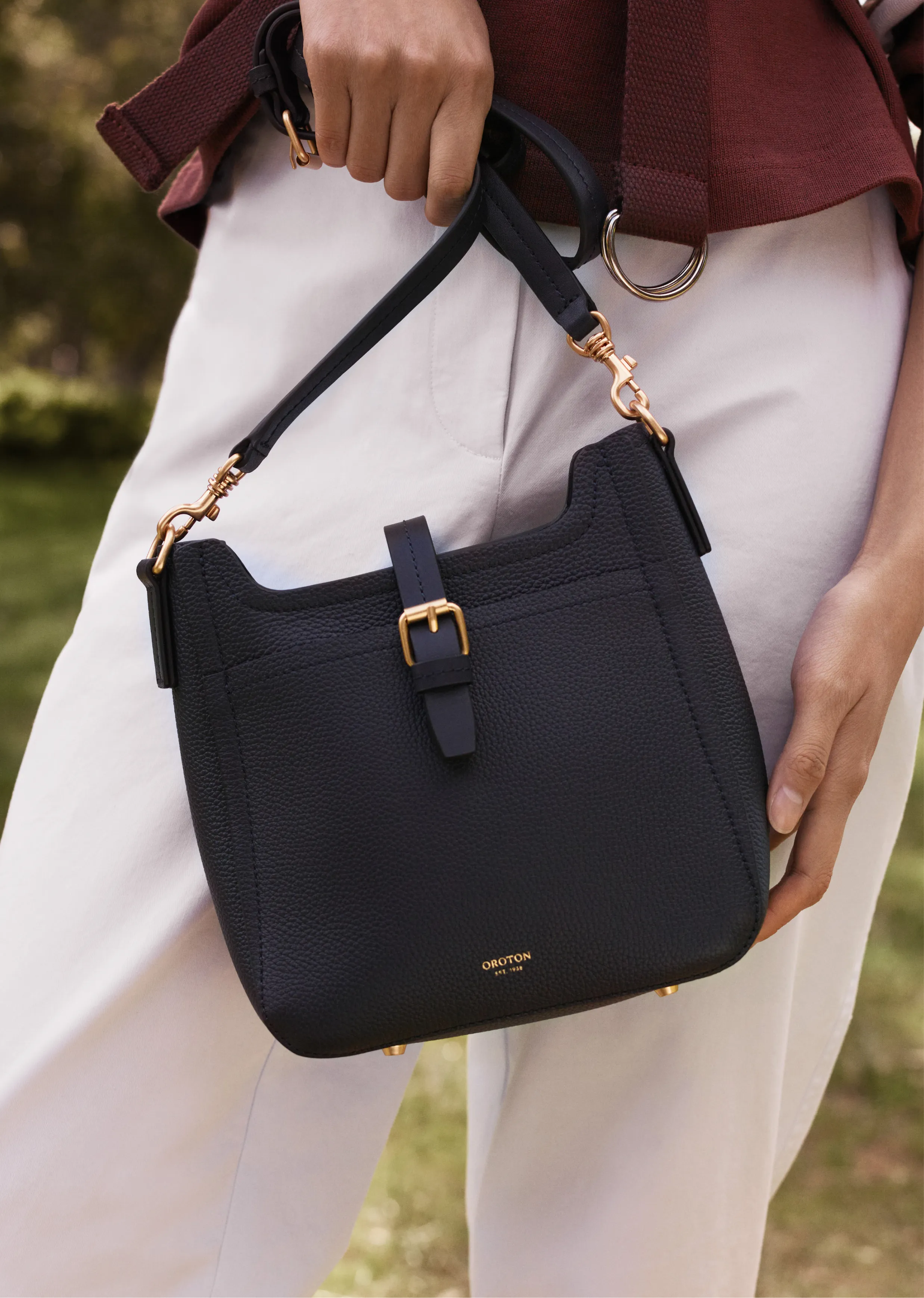 A person holding a navy blue handbag with a gold buckle.