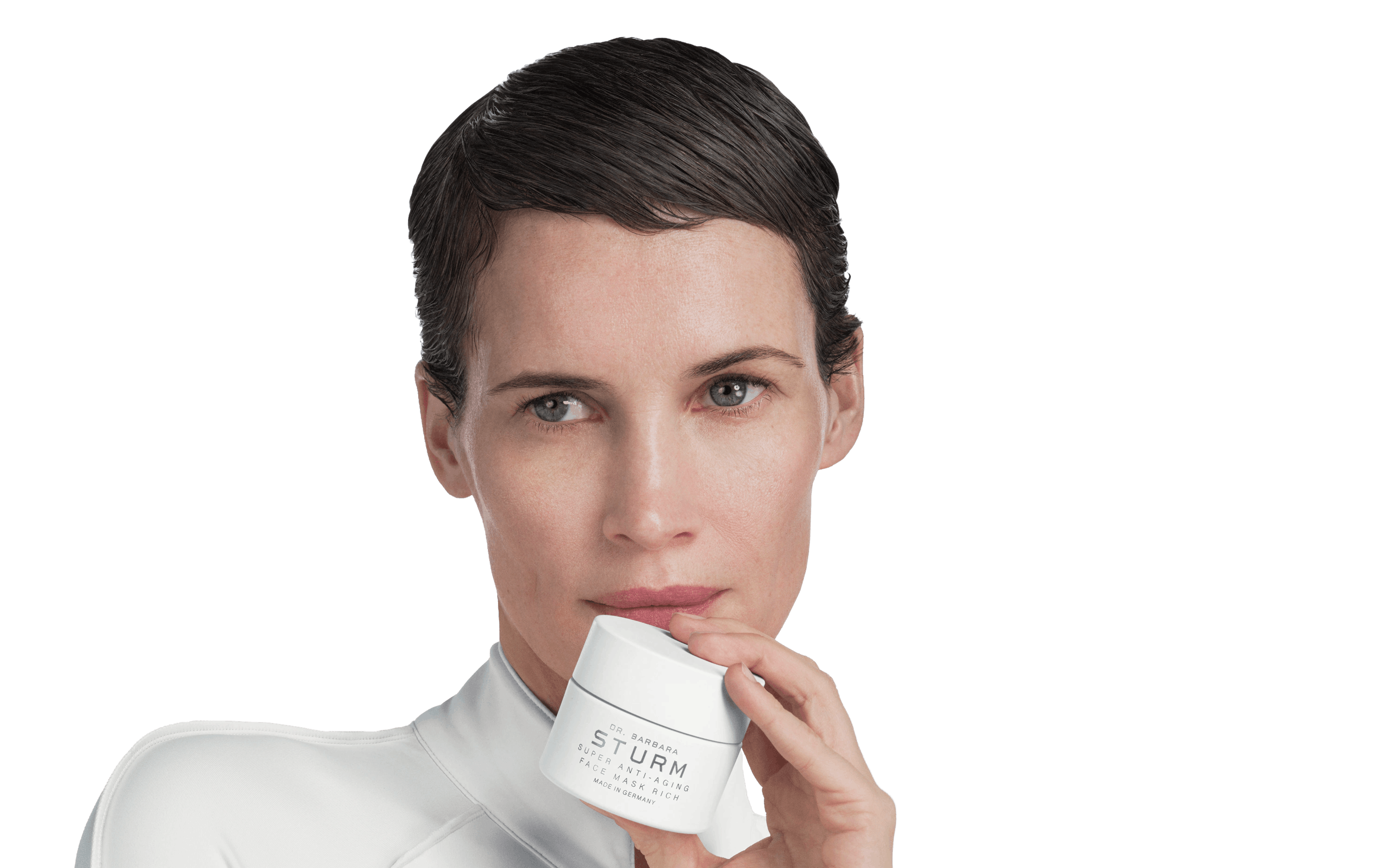 Woman holding a skincare product with a neutral expression.
