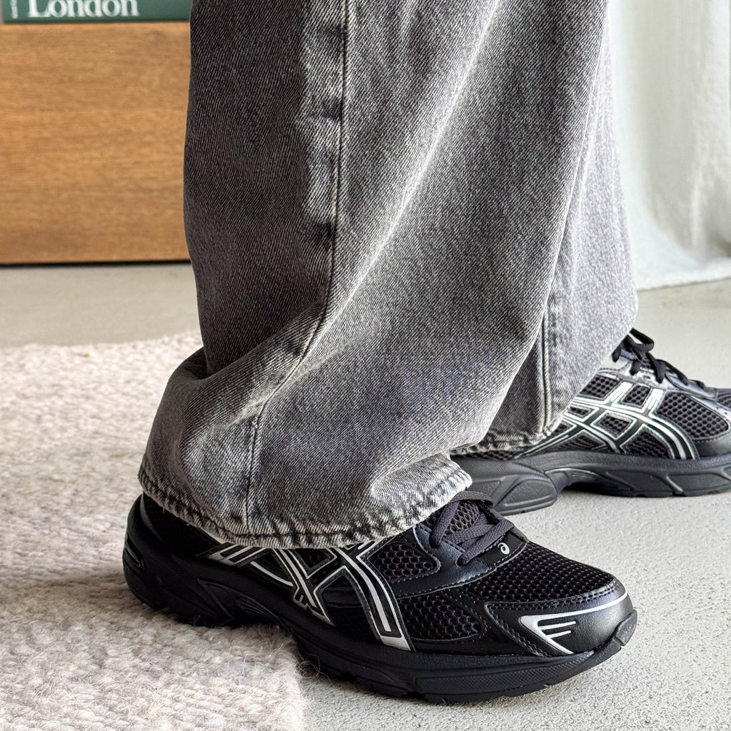 Person wearing gray jeans and black athletic shoes indoors.