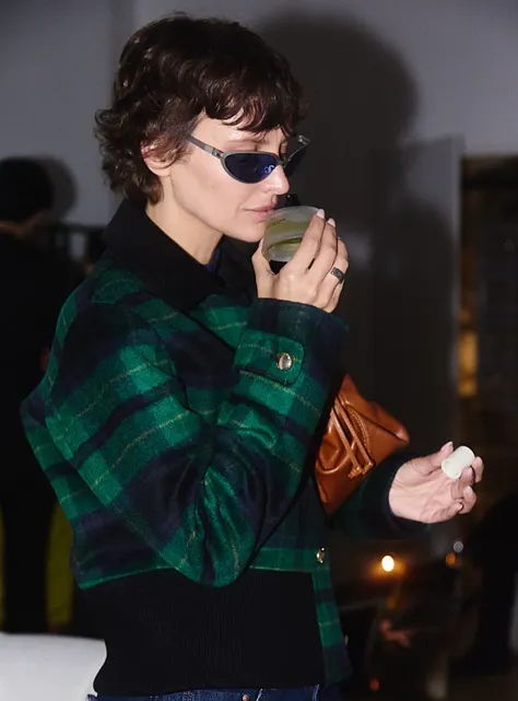 Person in sunglasses holding a drink and a small object.