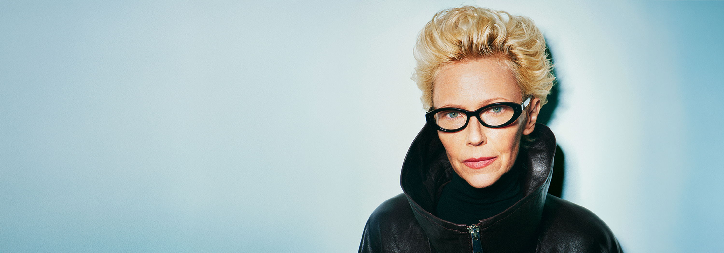 A person with stylish hair and Robert Marc glasses against a light blue background.