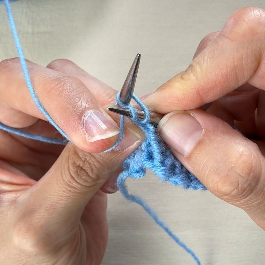 Linksverschränkt Stricken. Das Garn wird um die rechte Nadel gelegt.