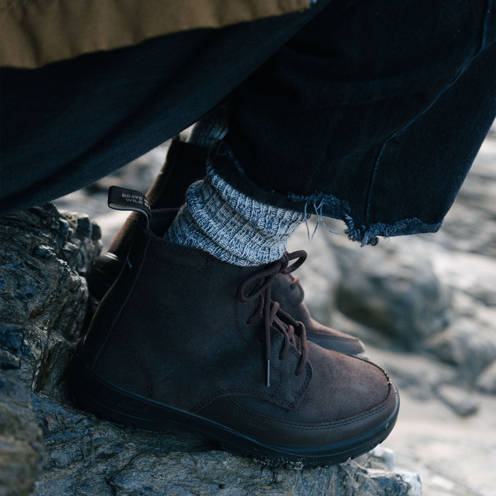A close-up of brown boots and patterned socks on rocky terrain.