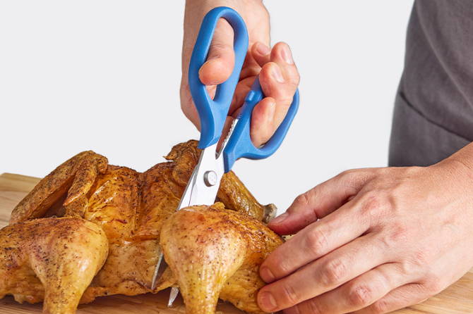 A chef using Blue Misen Kitchen Shears to separate a thigh cut from a cooked spatchcocked chicken.