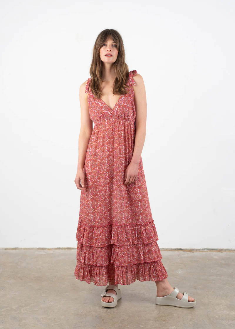 A model wearing a pink sleeveless dress with a paisley print and tiered detailing on the lower hem